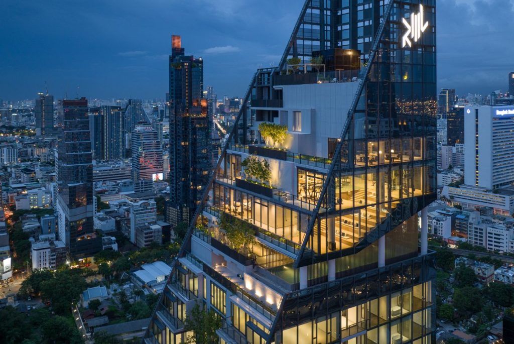 Dark glass tower top with lit terraces above dense Bangkok skyline at dusk