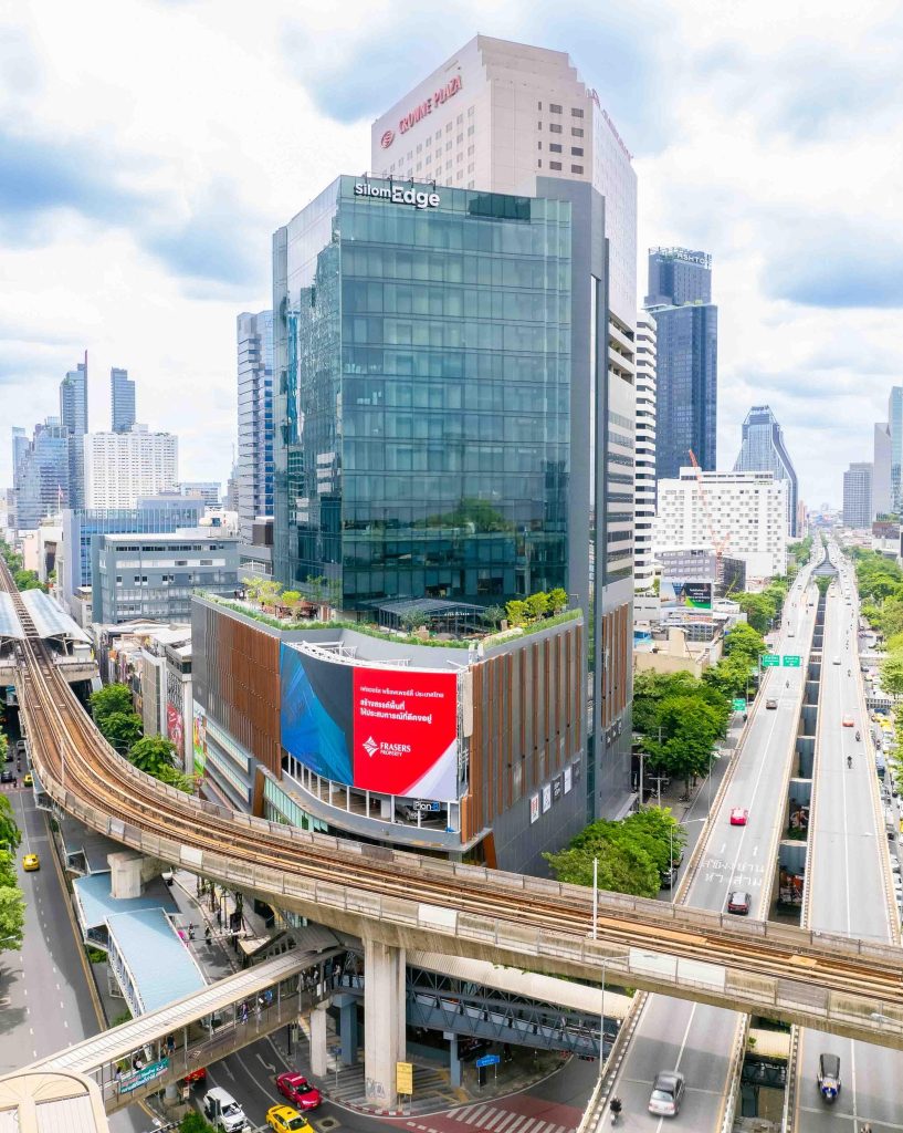 Street-level glass office and retail complex beside BTS tracks and elevated road, daytime