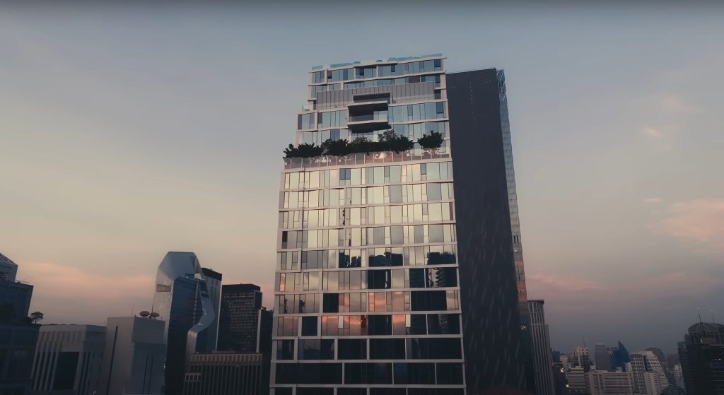 Dark glazed residential tower with planted rooftop against hazy sky, other towers behind