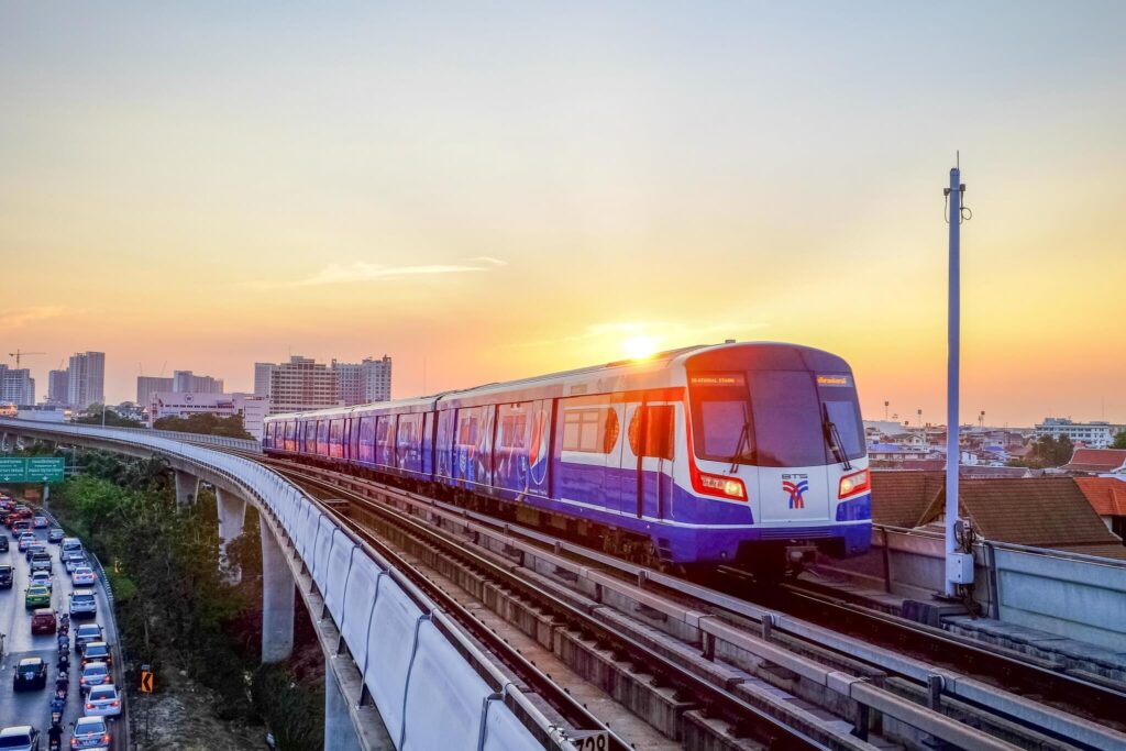 BTS Skytrain on an elevated track beside a busy road at sunset