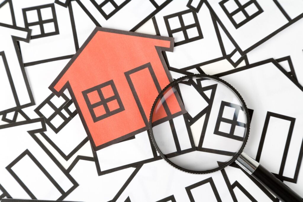 Magnifying glass over a red paper house among black and white house outlines
