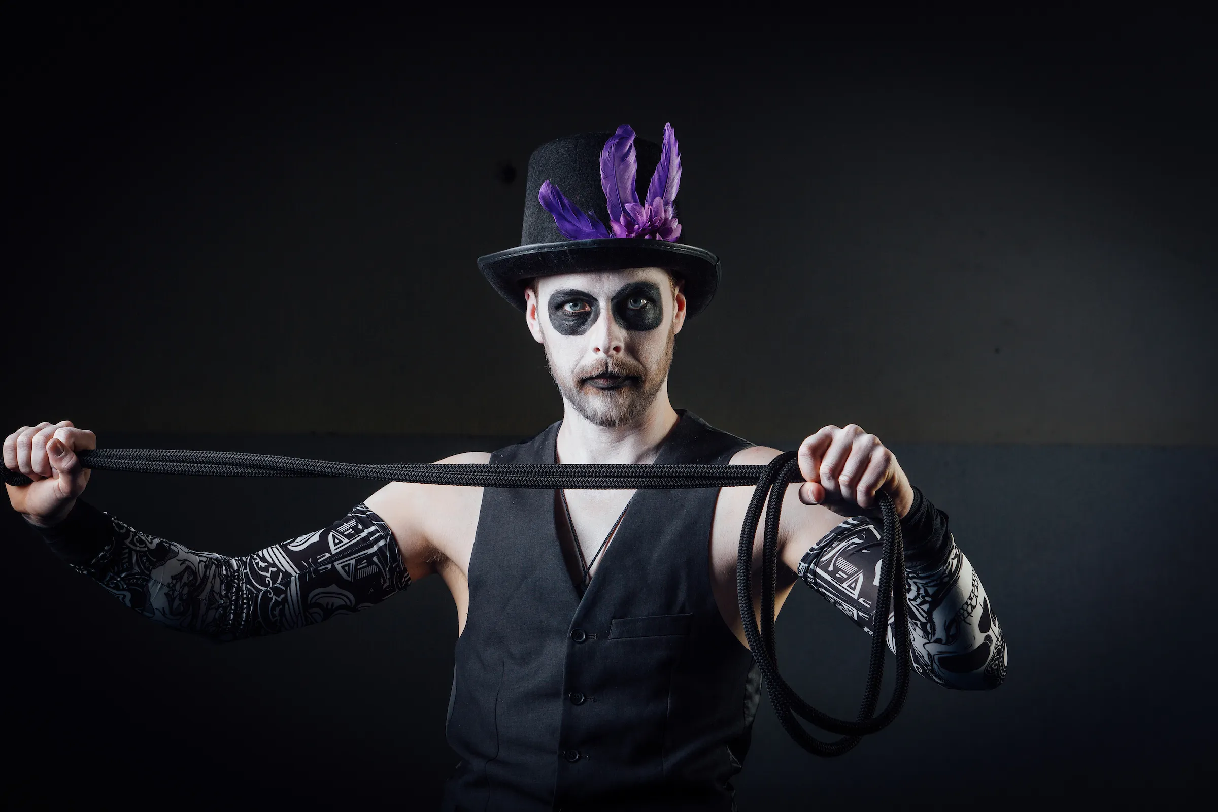 Circus performer in skull face paint and a feathered top hat holding a long black whip.