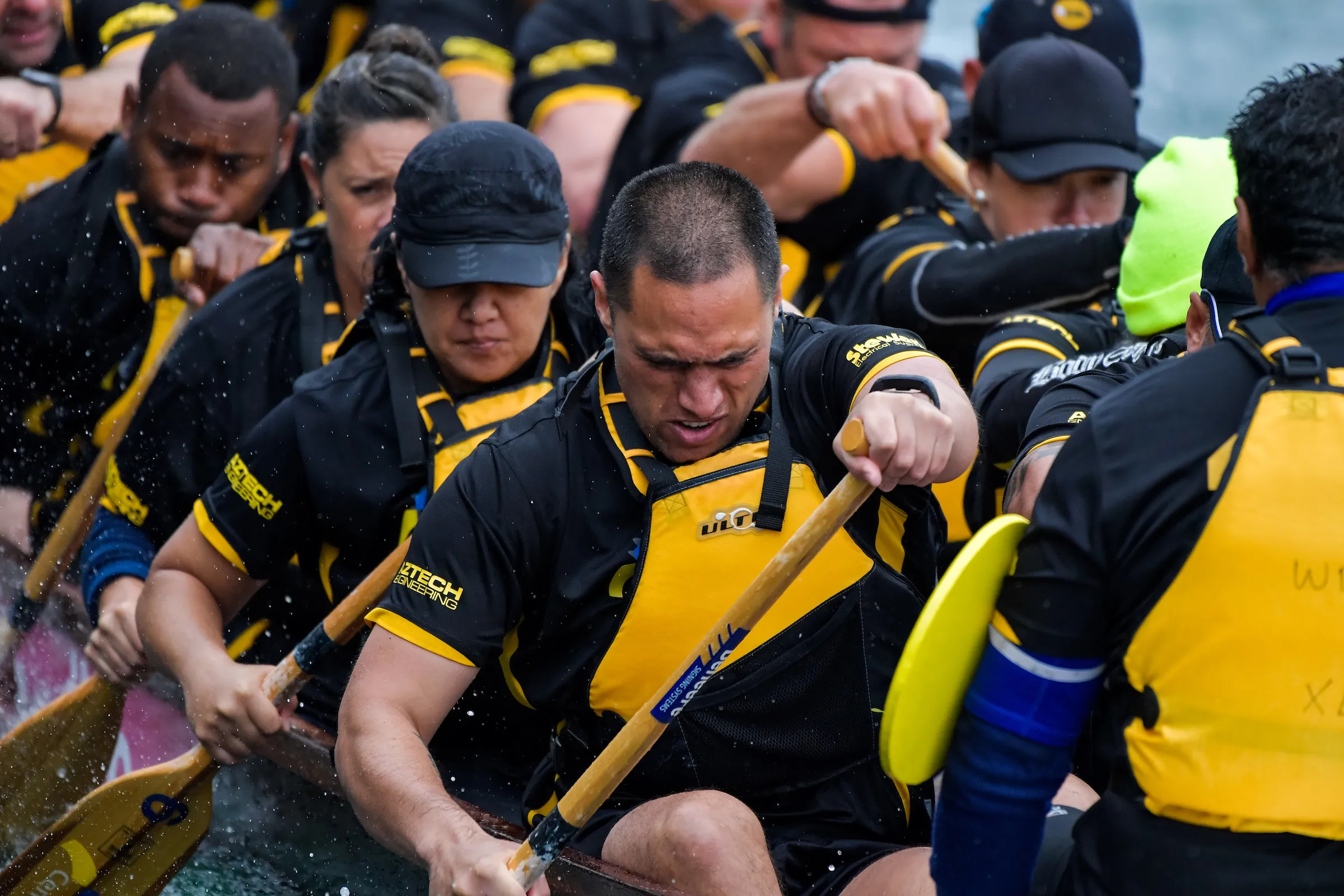 Dragon boat crew in black and yellow uniforms paddling hard during a race.