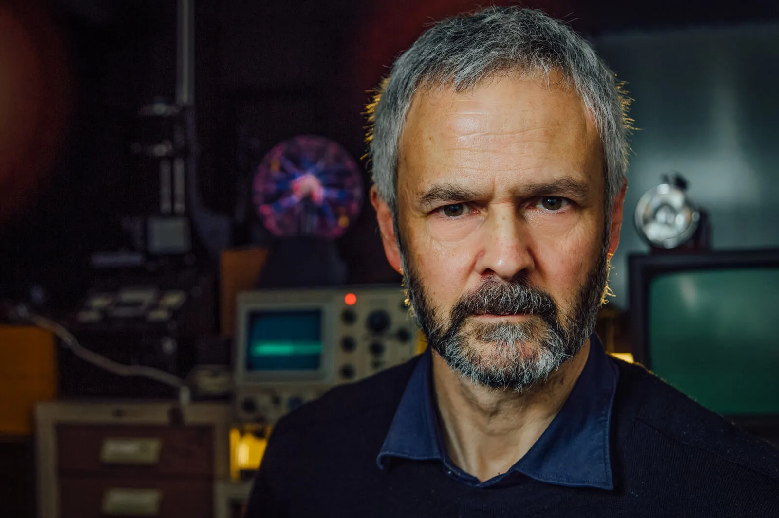 Bearded man photographed among electronic laboratory equipment.