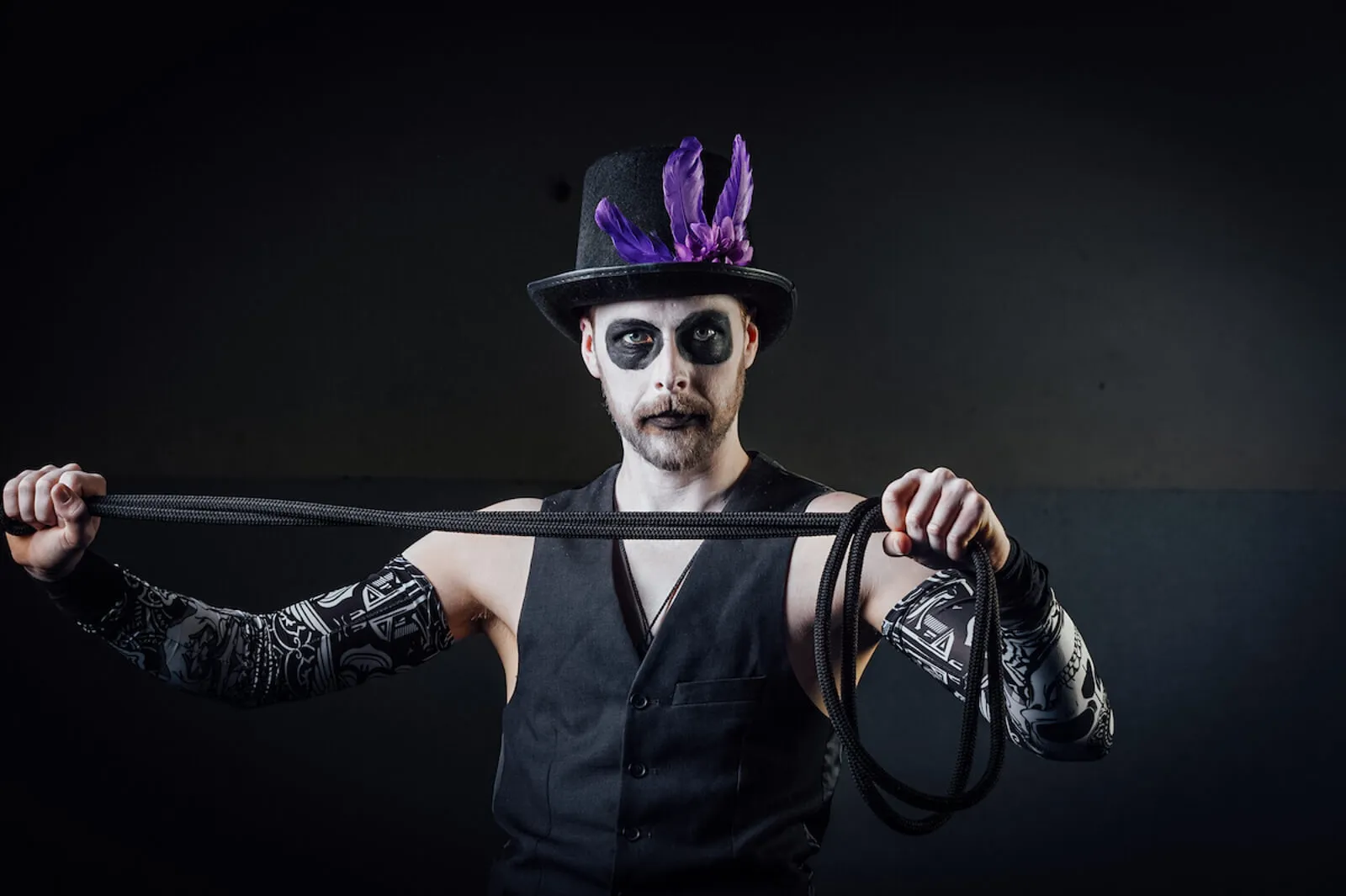 Performer in skull face paint and a feathered top hat holding a long black whip.