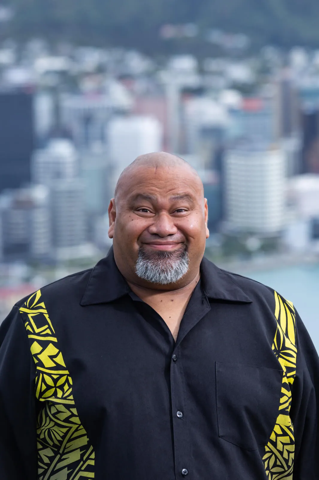 Smiling man in a black and yellow patterned shirt with Wellington city blurred behind him.