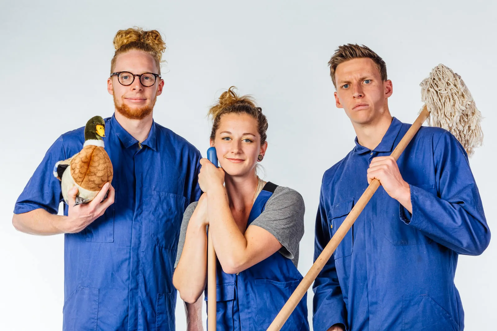 Three people in blue work overalls posing with cleaning tools and a soft toy.