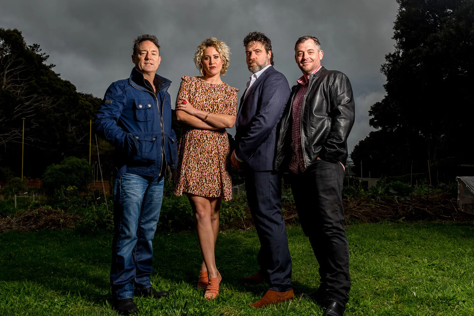 Four adults posing together on a lawn beneath a dramatic cloudy sky.
