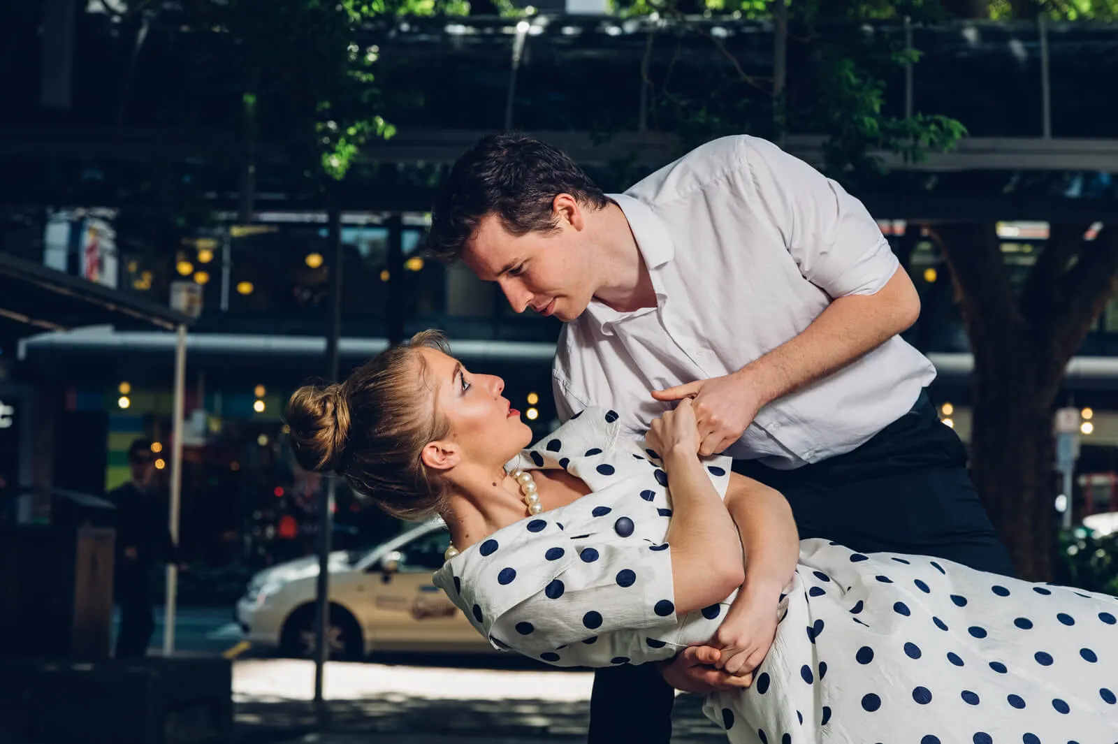 Man dipping a woman in a polka-dot dress on a city street.