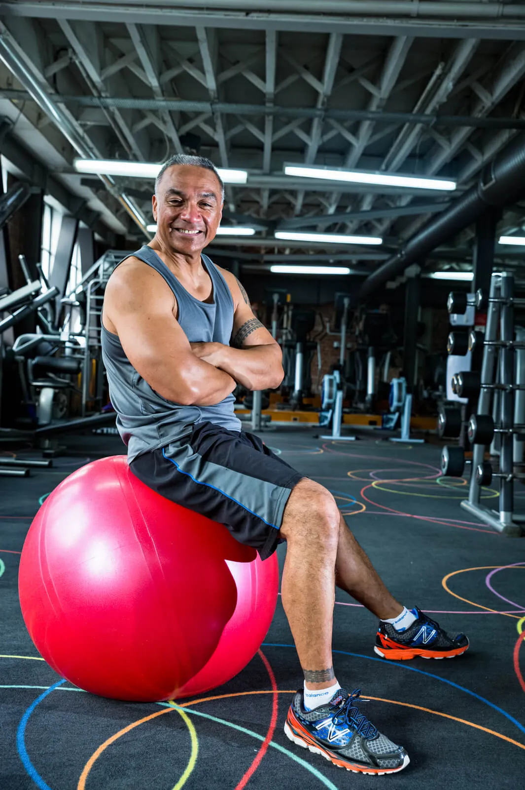 Smiling man seated on a red exercise ball in a gym.