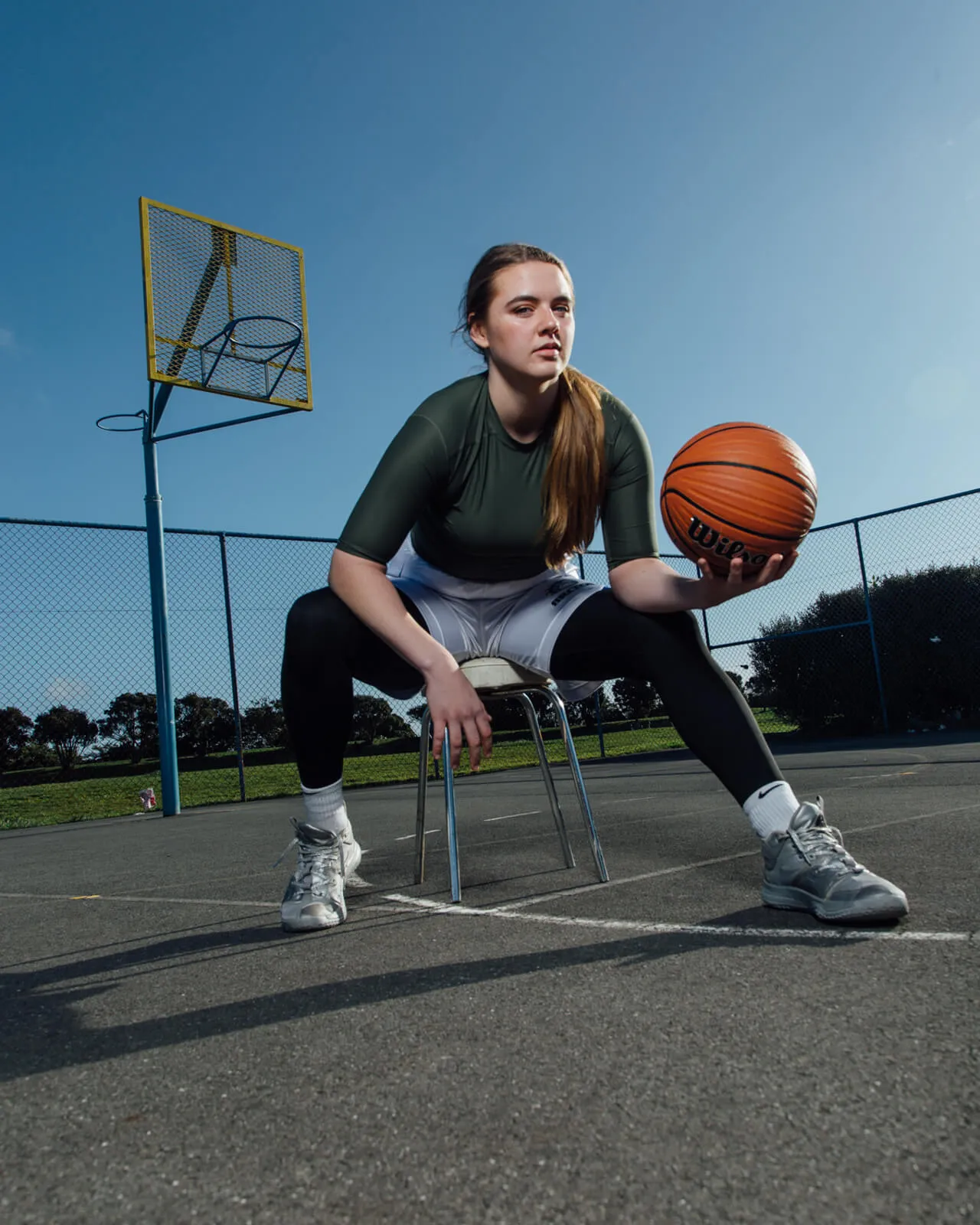 Basketball player seated on a chair holding a ball on an outdoor court.