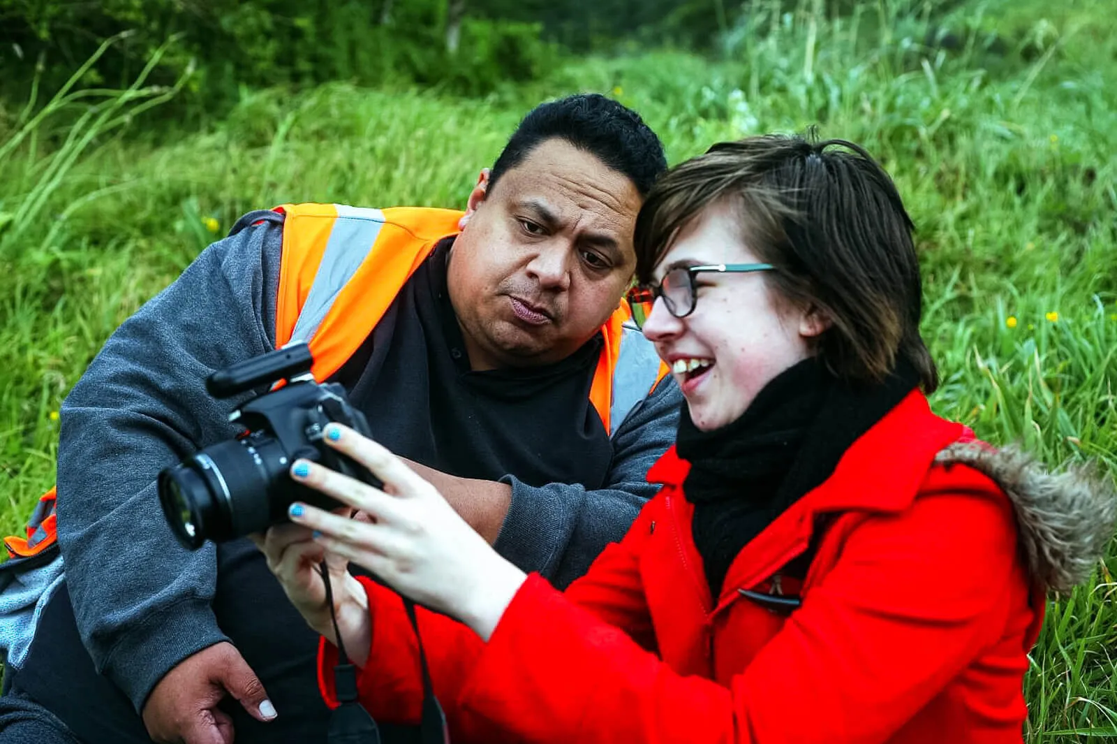 Photography mentor reviewing an image on a camera with a smiling student outdoors.