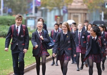 Group of students in school uniforms walking outdoors on a pathway, smiling and chatting.