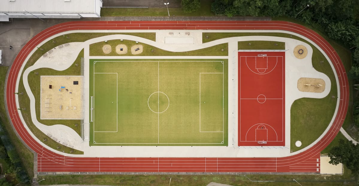 Aerial view of a sports complex with a green soccer field, red basketball court, and surrounding running track.