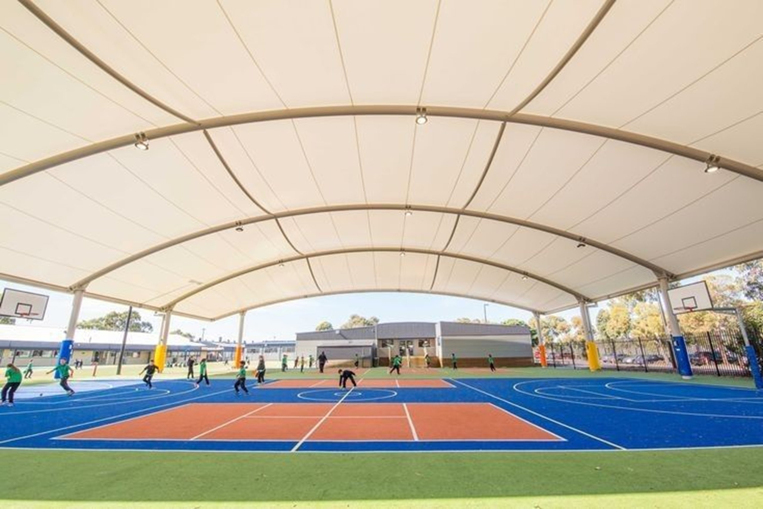 Covered outdoor basketball and netball court with children playing under a large white canopy.