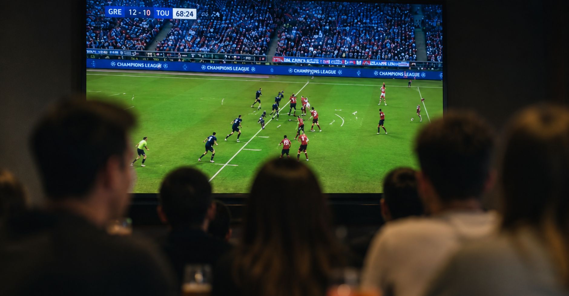 Groupe de personnes regardant un match de football de Ligue des champions sur écran géant, silhouettes de dos en salle tamisée