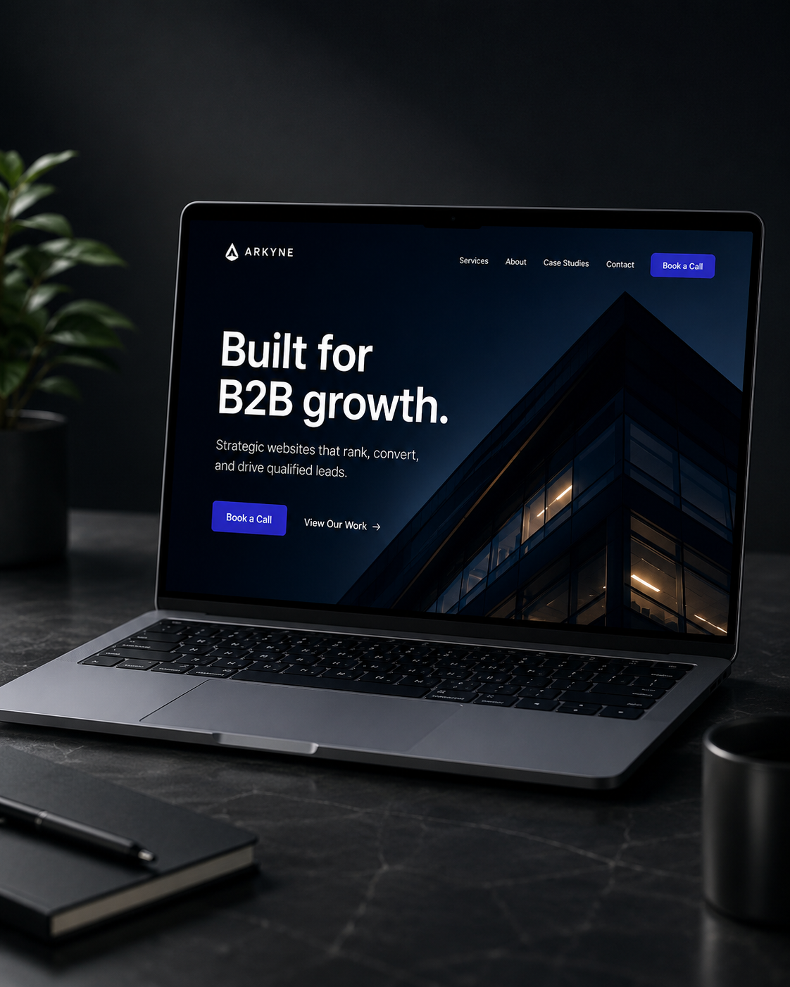 Laptop on desk showing a website homepage for B2B growth with a dark building image and call-to-action buttons.