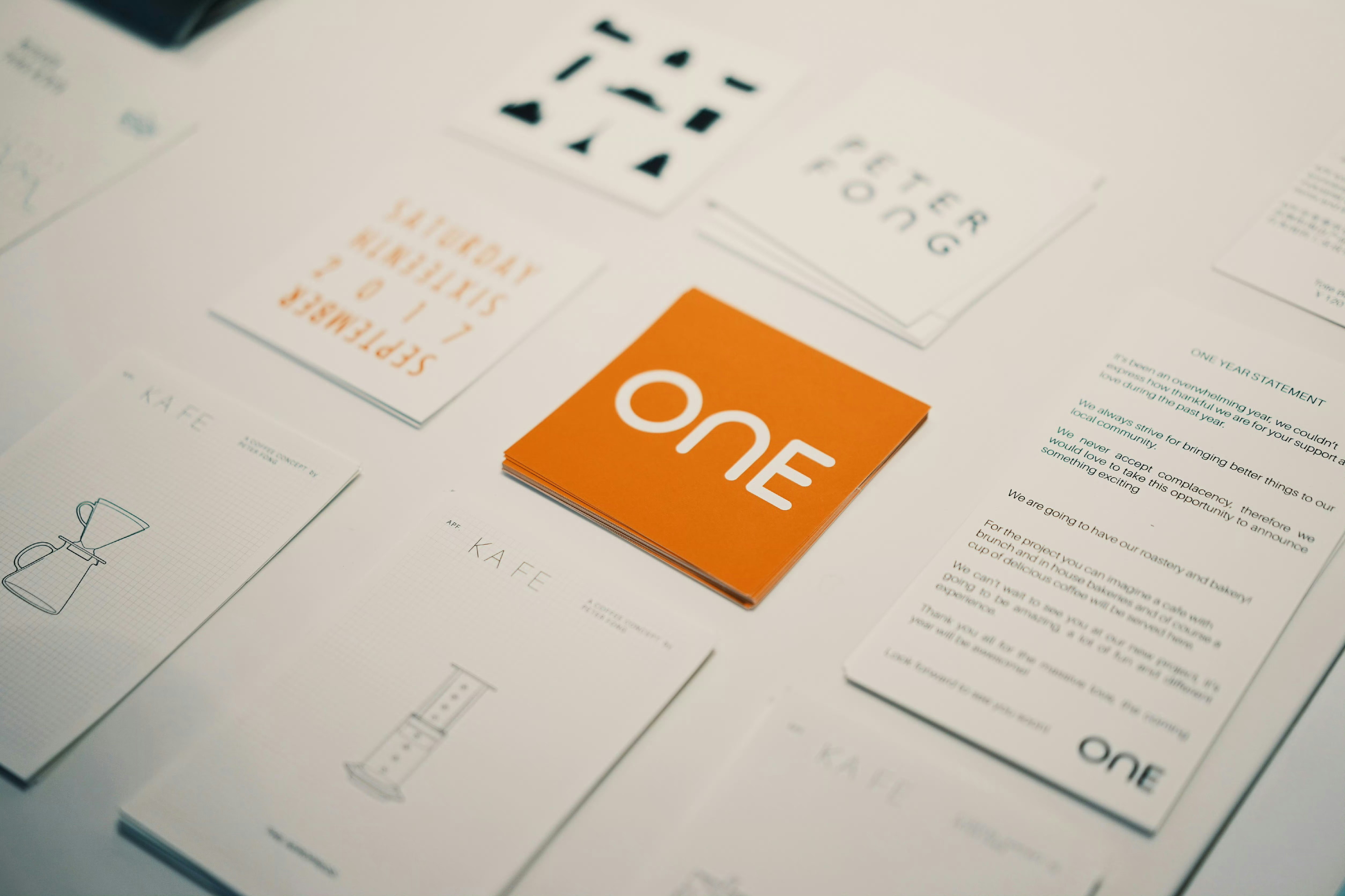 Stack of orange cards with white text ONe surrounded by white papers with text and illustrations on a table.