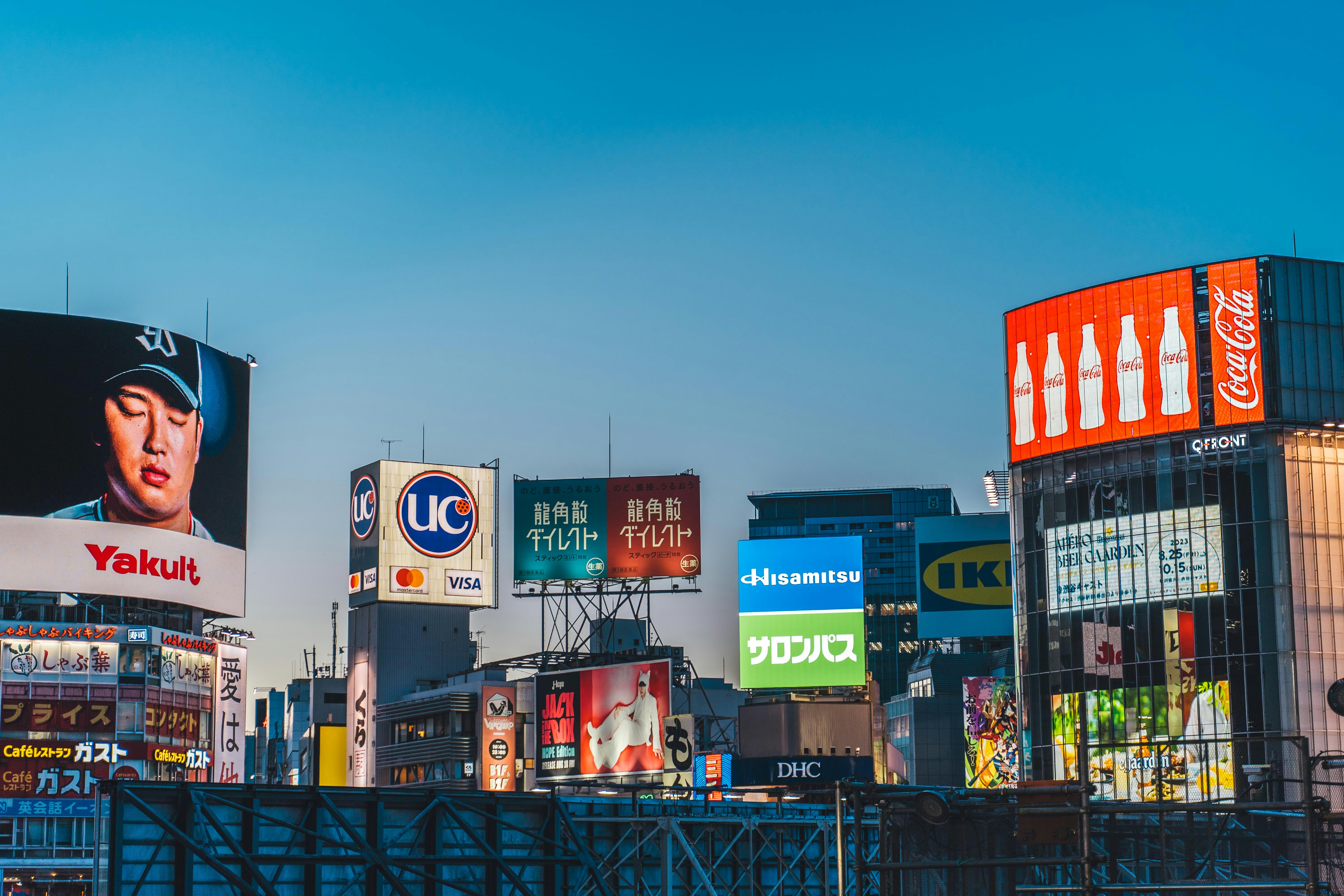 Cityscape with illuminated billboards including Coca-Cola, Yakult, UC, and IKEA during dusk.