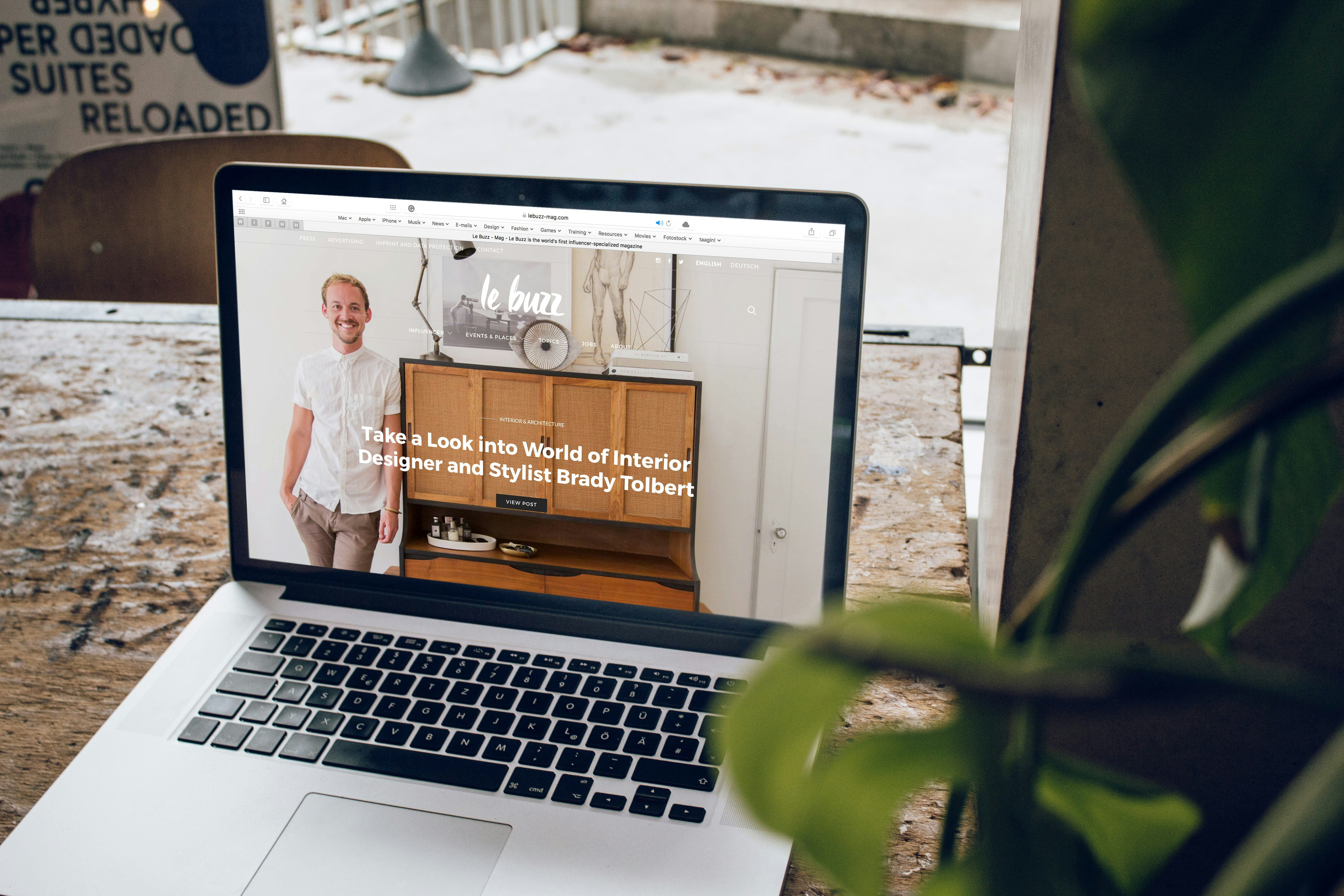 Laptop on table displaying website featuring interior designer Brady Tolbert with wooden furniture background.