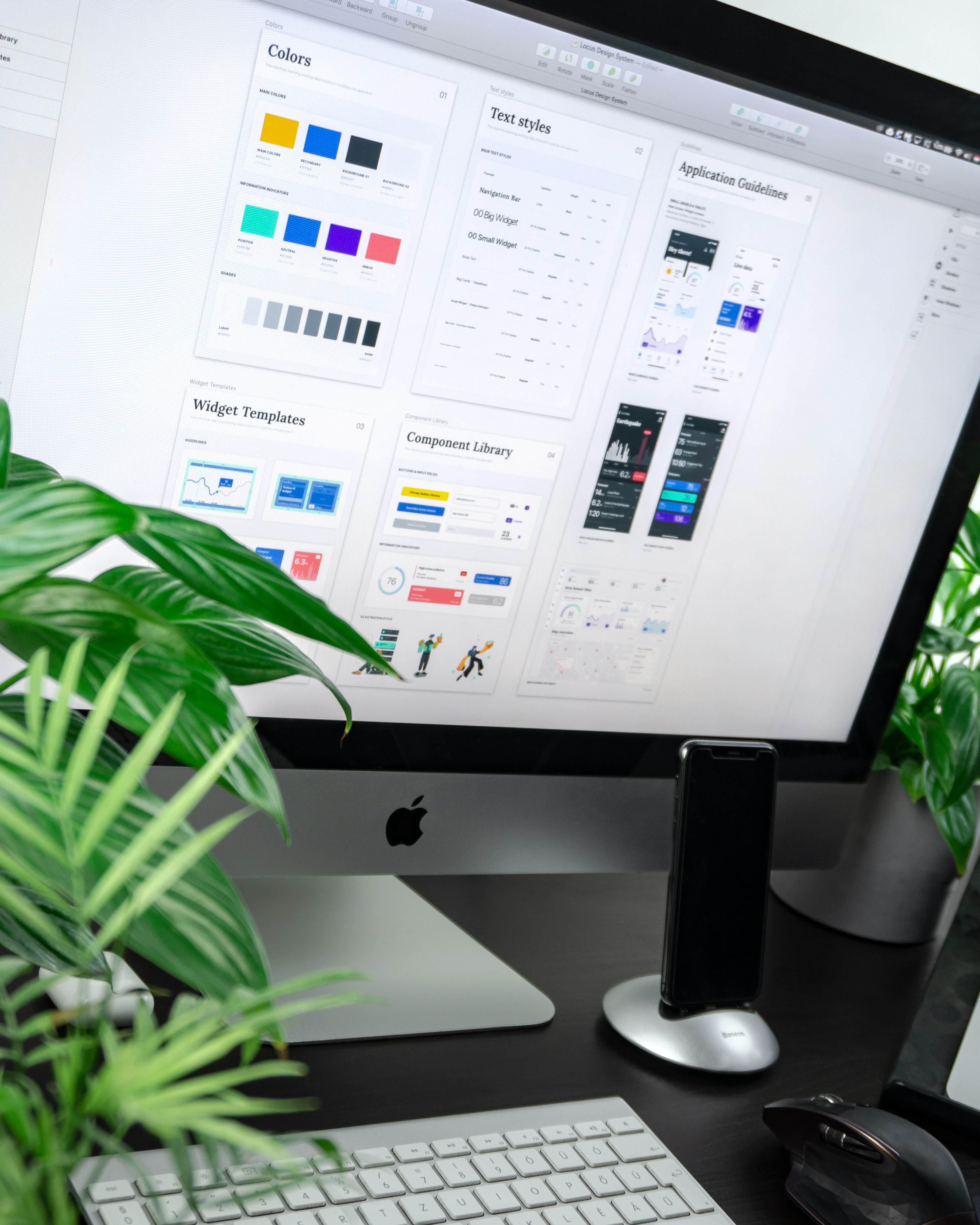 Desktop setup with an iMac showing UI design templates and plants beside keyboard and mouse.