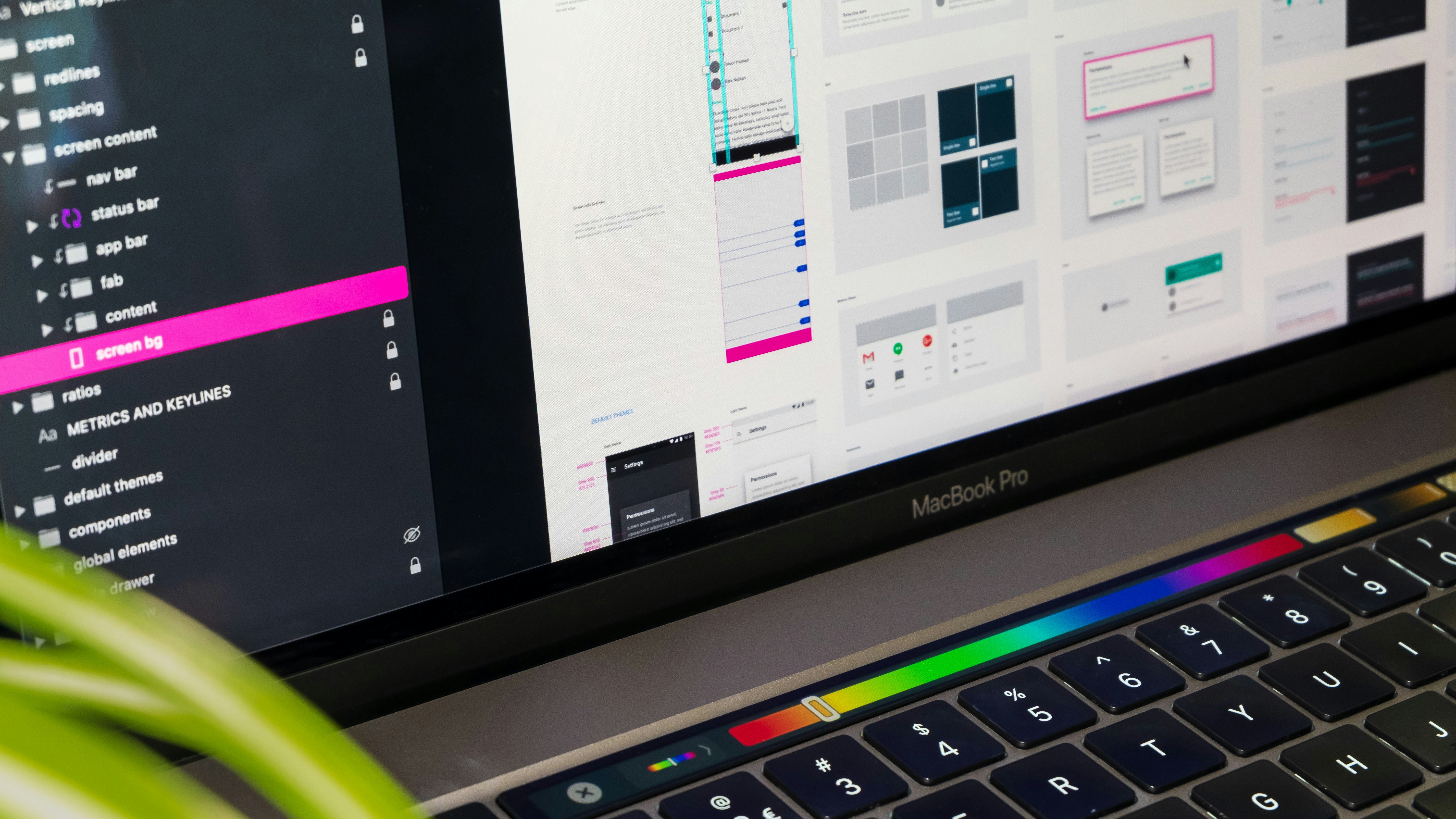 Close-up of MacBook Pro screen showing UI design software with color bar and file layers visible.