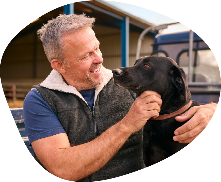 A man smiles at his black working dog in a farm yard.