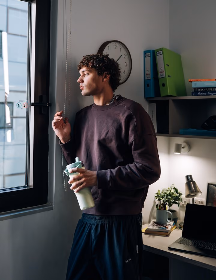 A student standing with a drink in his room