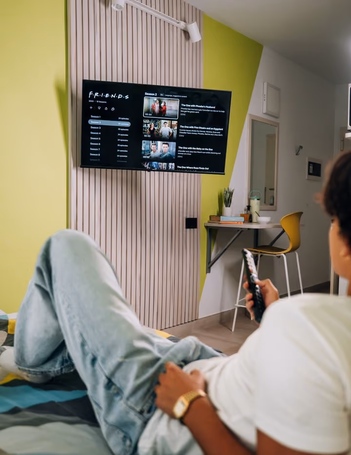 A student watching the wall-mounted television from the bed