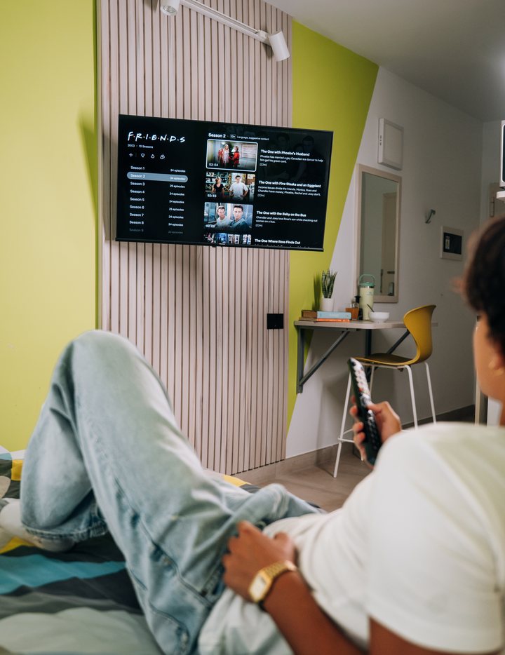 A student watching the wall-mounted television from the bed