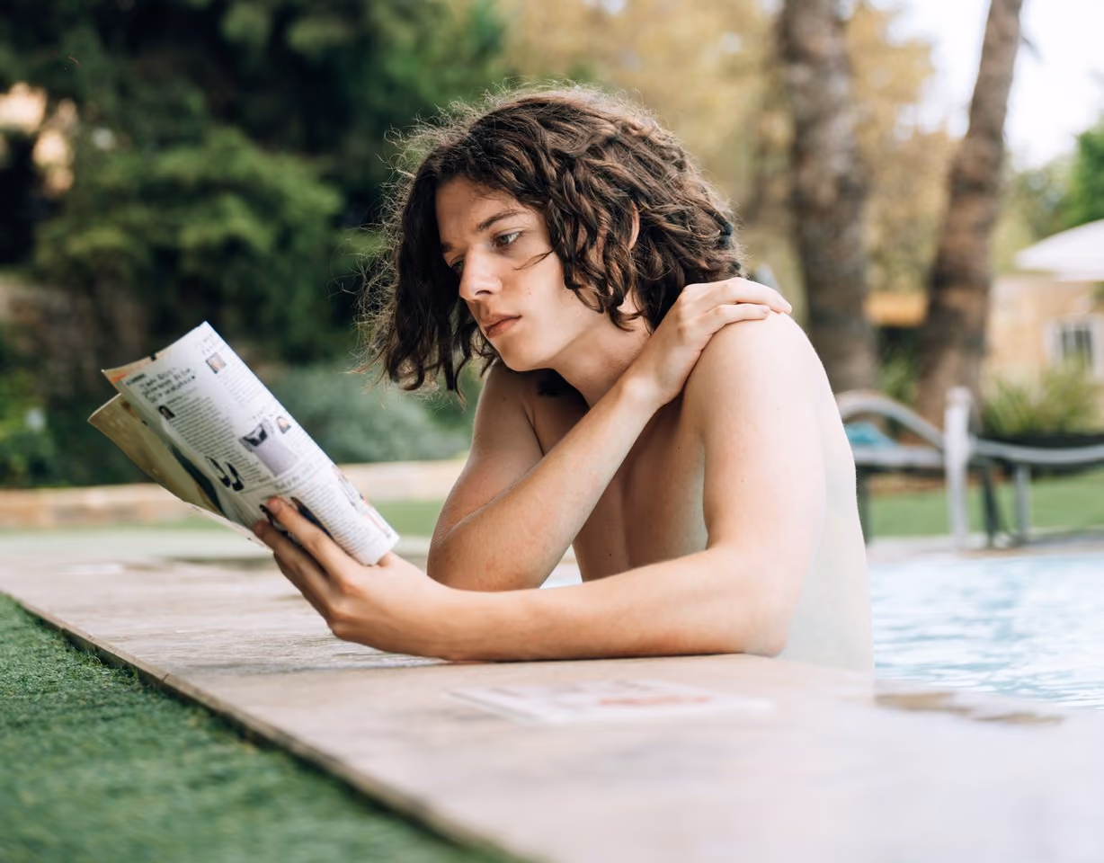 A student reading a magazine beside the pool