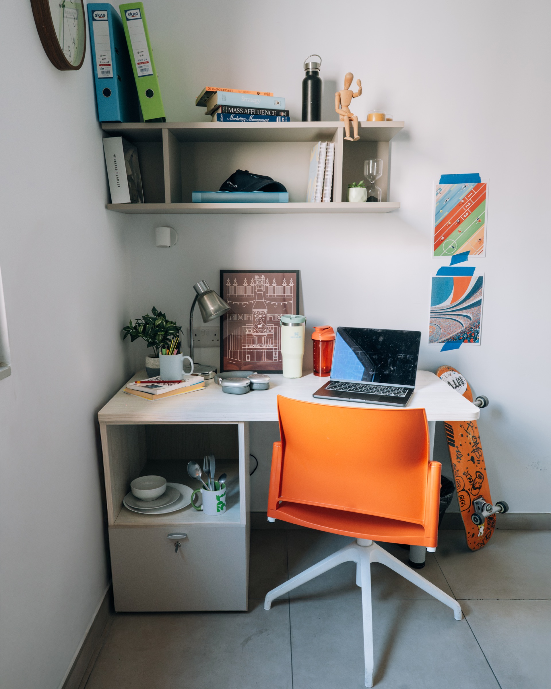 Corner desk in a Cosy room with a laptop, an orange swivel chair and a wall shelf of books and folders