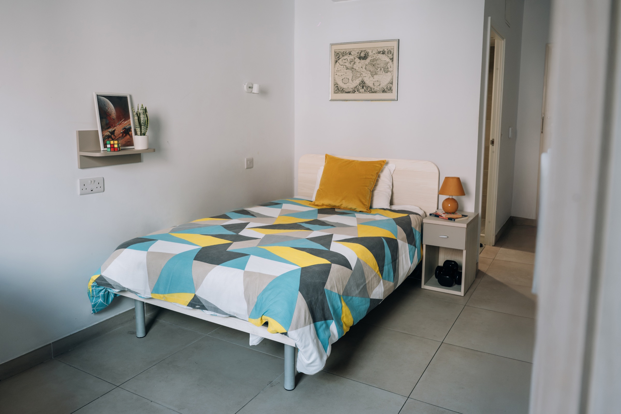 Single bed in a Cosy room made up with a patterned duvet, beside a bedside table and lamp