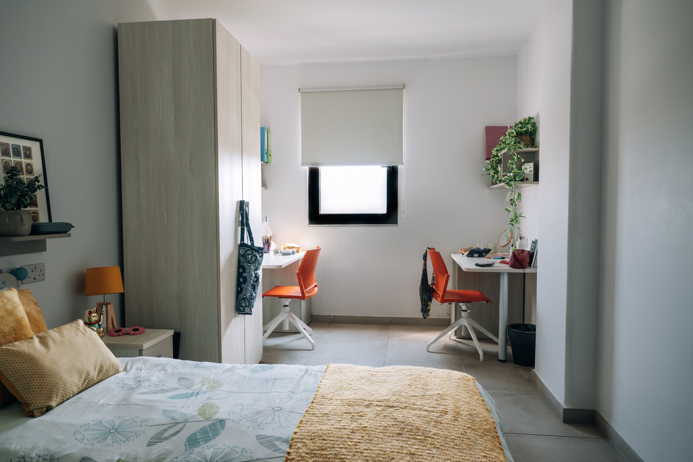 Social room seen from the bed, with two desks, orange chairs and a full-height wardrobe