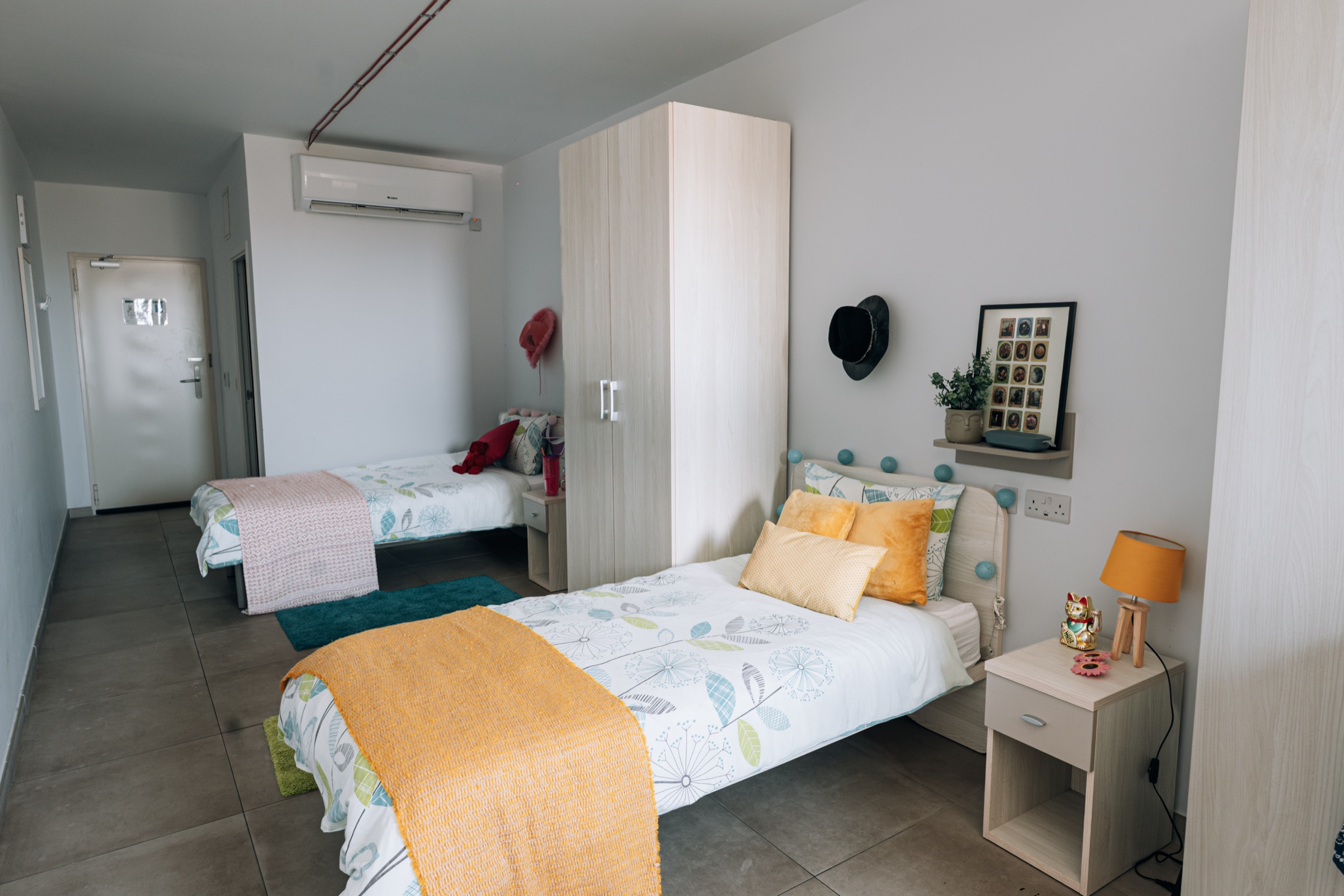 Two single beds in a Social room, separated by a wardrobe, with the entrance door beyond