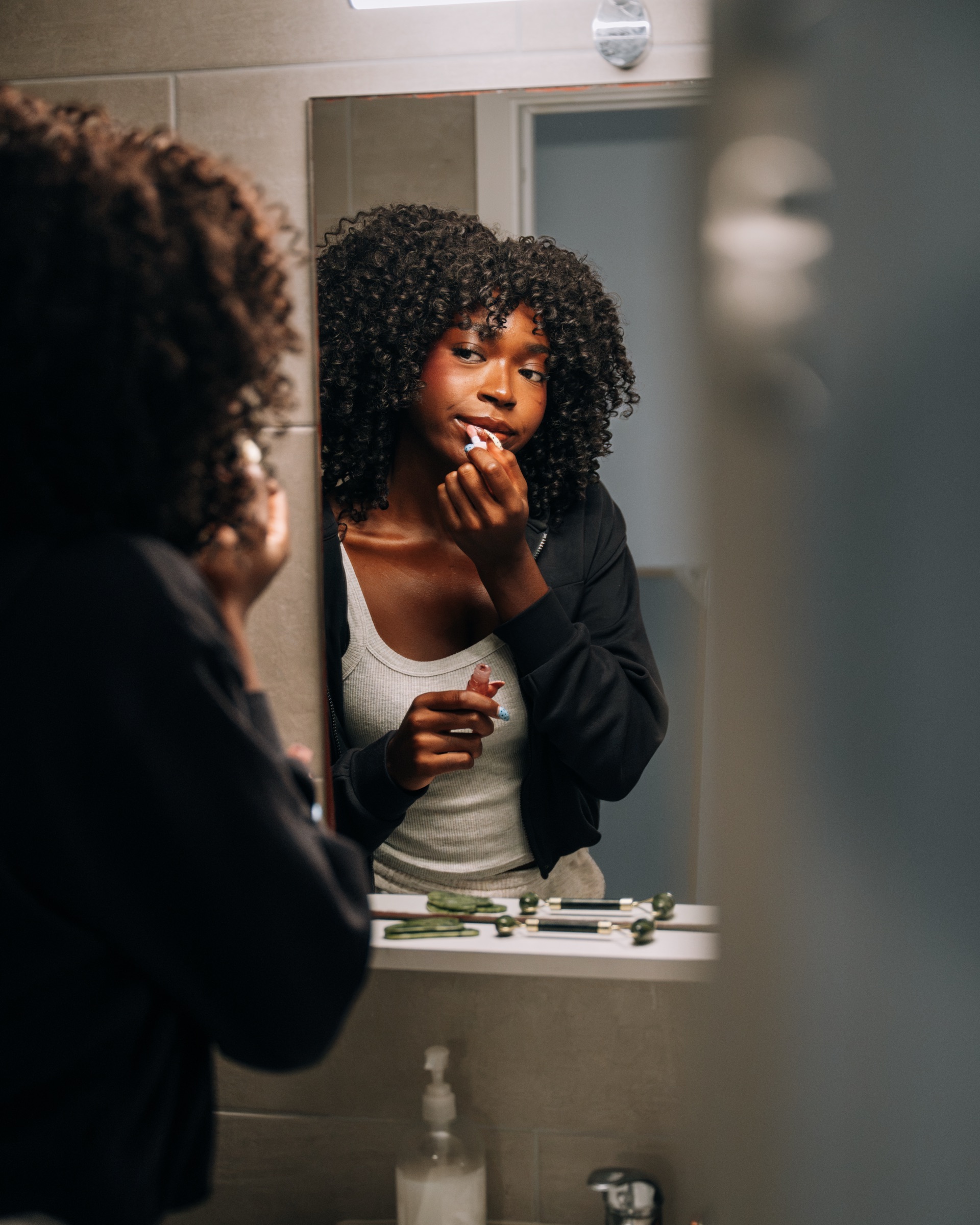 Student putting on lip balm at the mirror of a Social room bathroom