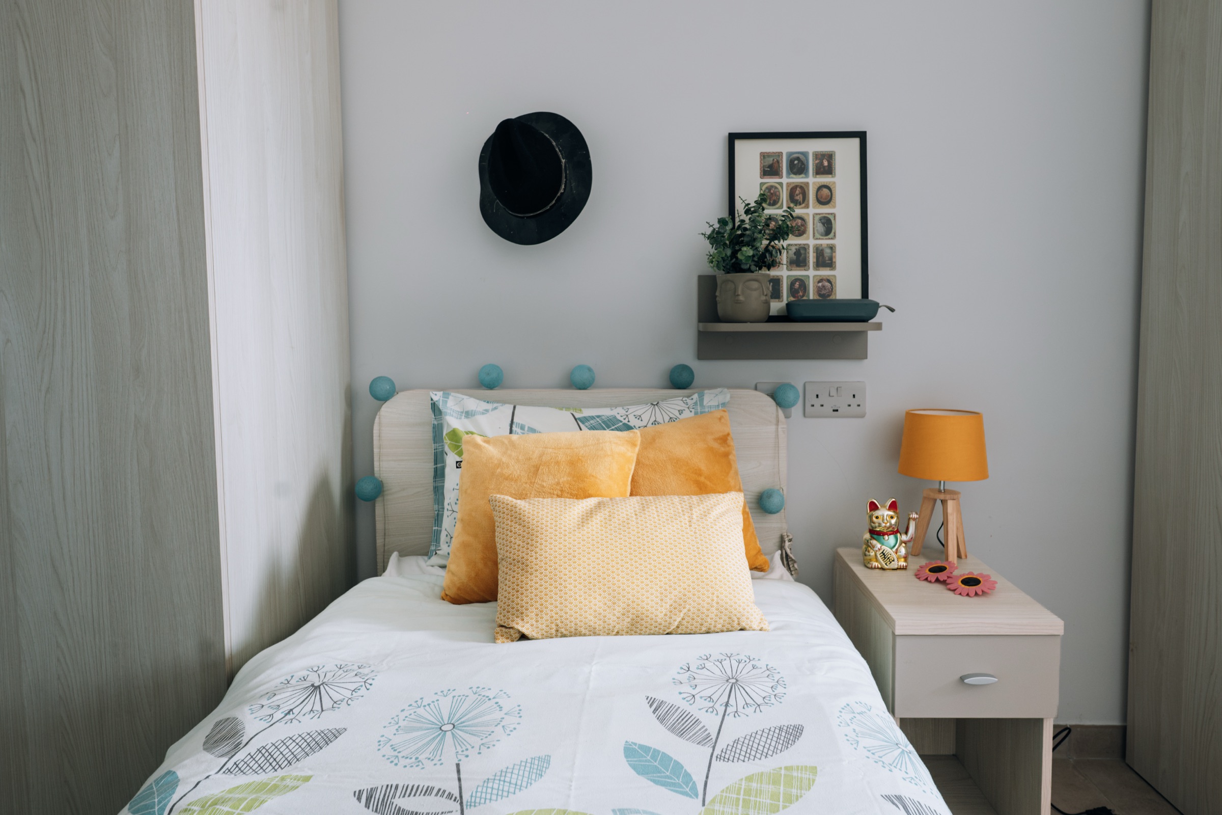 Made-up single bed in a Social room with cushions, a bedside lamp and a shelf above the headboard