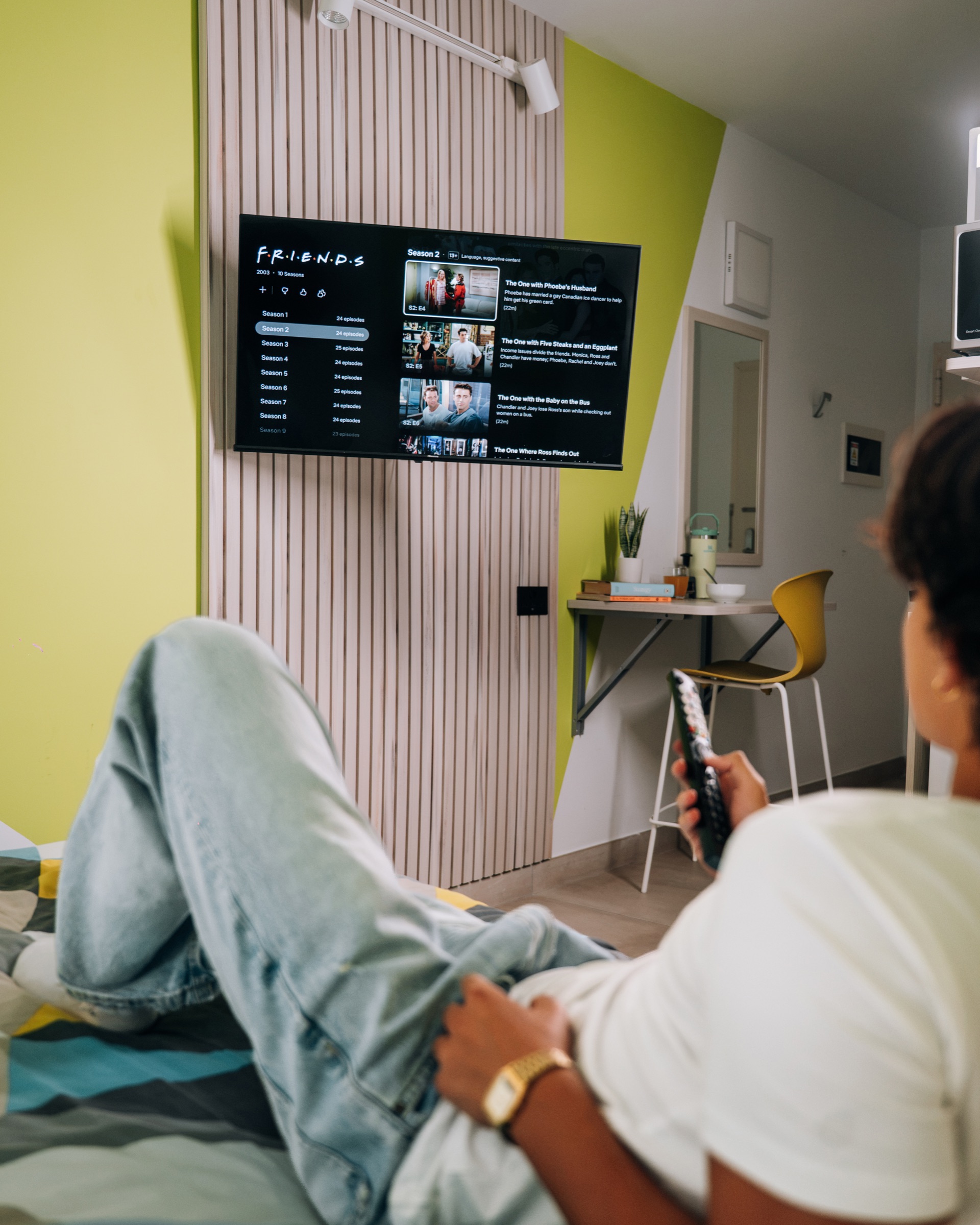 Student lying on the bed in a Solo room watching the wall-mounted television