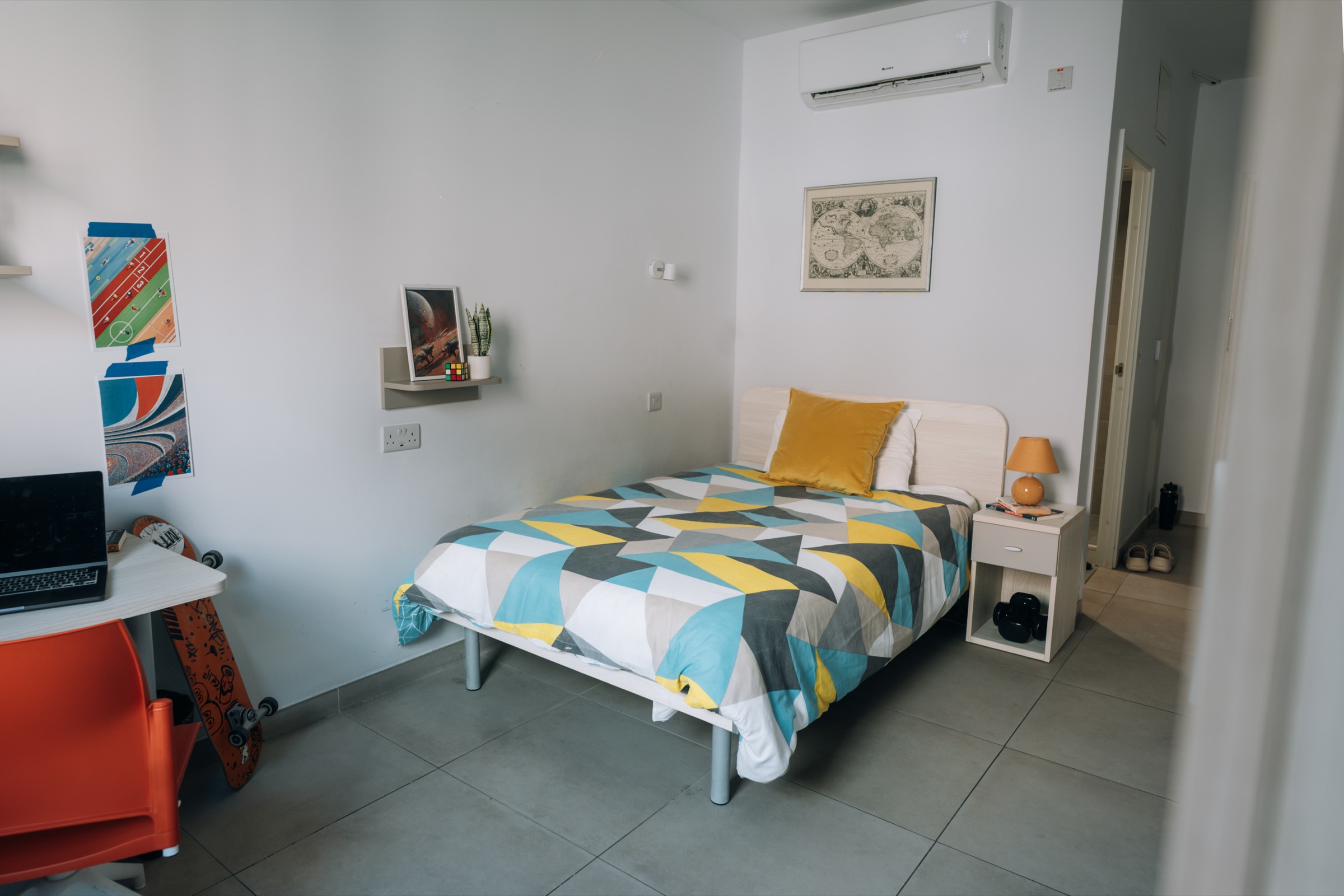 Cosy room with a single bed, air conditioning above it and the desk and skateboard by the door