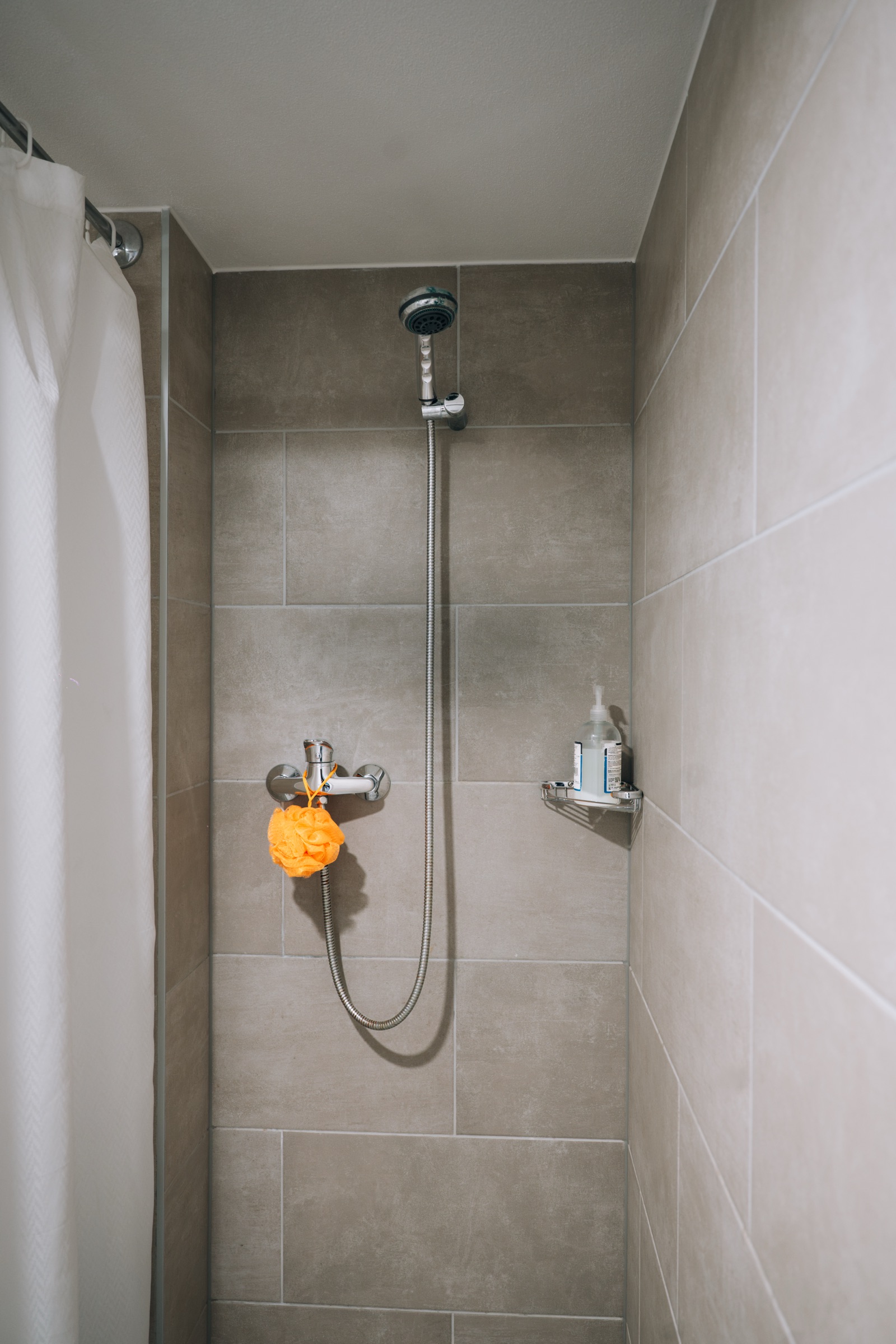 Tiled shower cubicle with a hand-held shower head and a shelf of toiletries