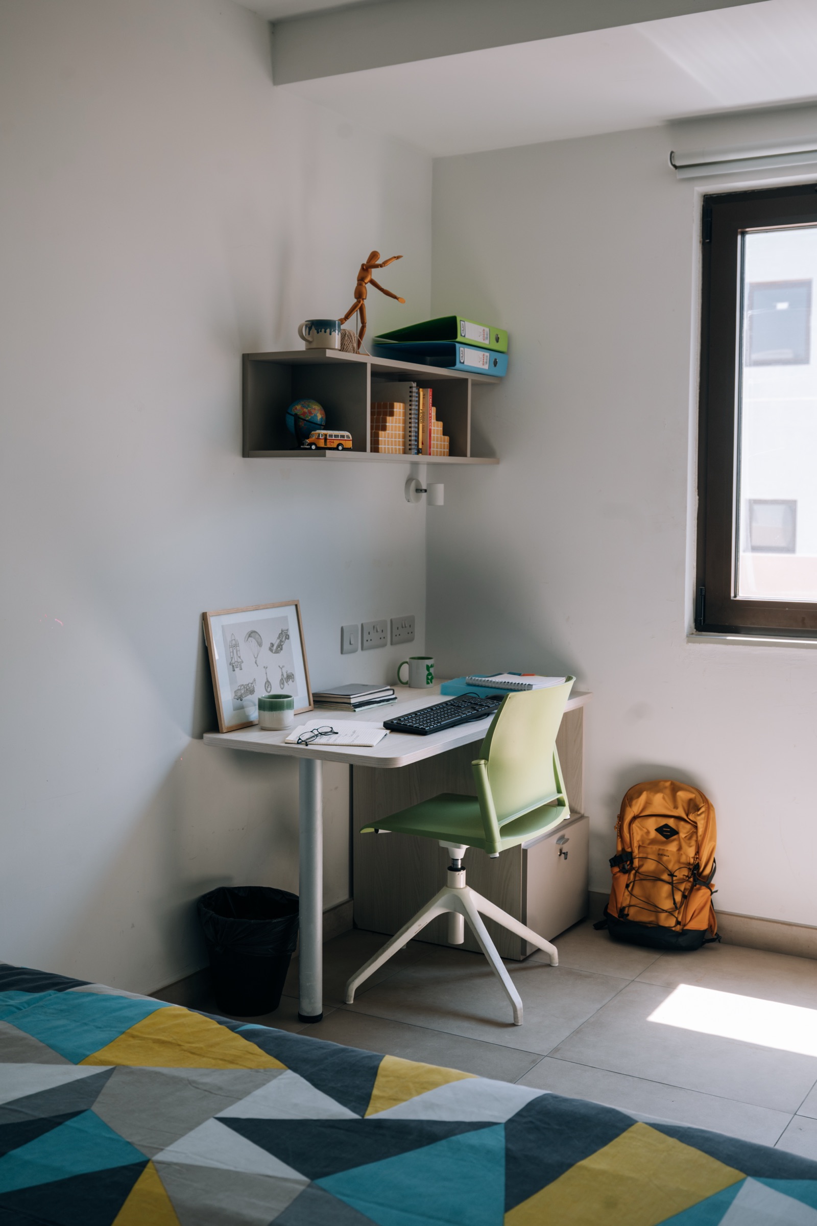 Desk and wall shelf in a Solo room, with a rucksack on the floor beside the window