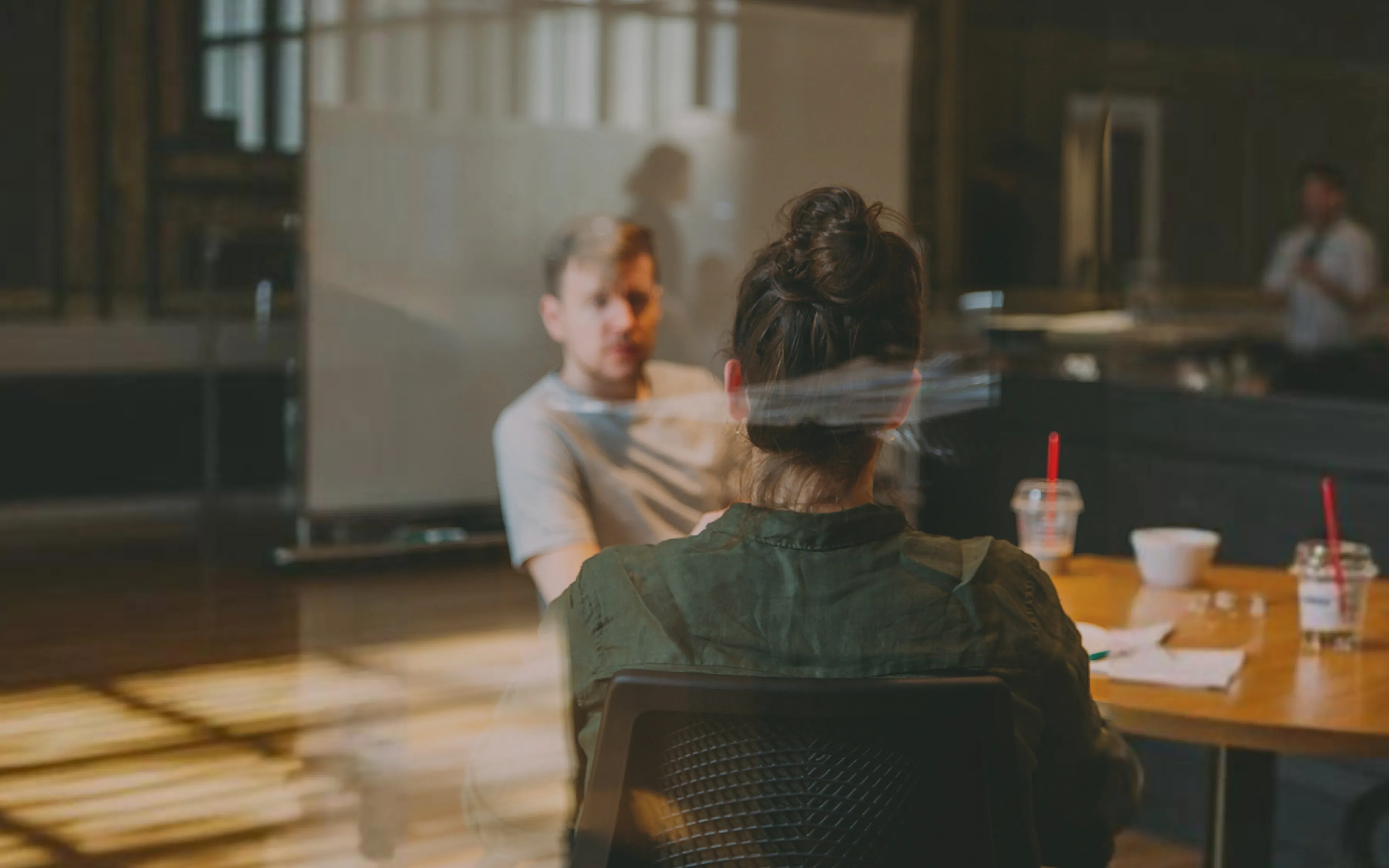 Zwei Personen im Gespräch an einem Besprechungstisch im Büro, durch eine Glasscheibe fotografiert