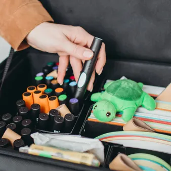 Hand greift nach bunten Stiften in einer Materialbox mit Coaching-Utensilien
