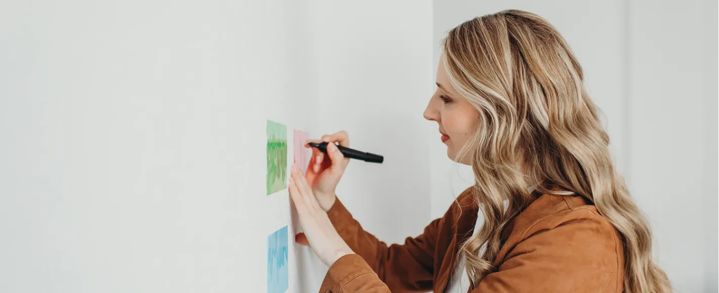 Melanie Bosse beschriftet Klebe-Zettel auf einer Wand mit einem Stift