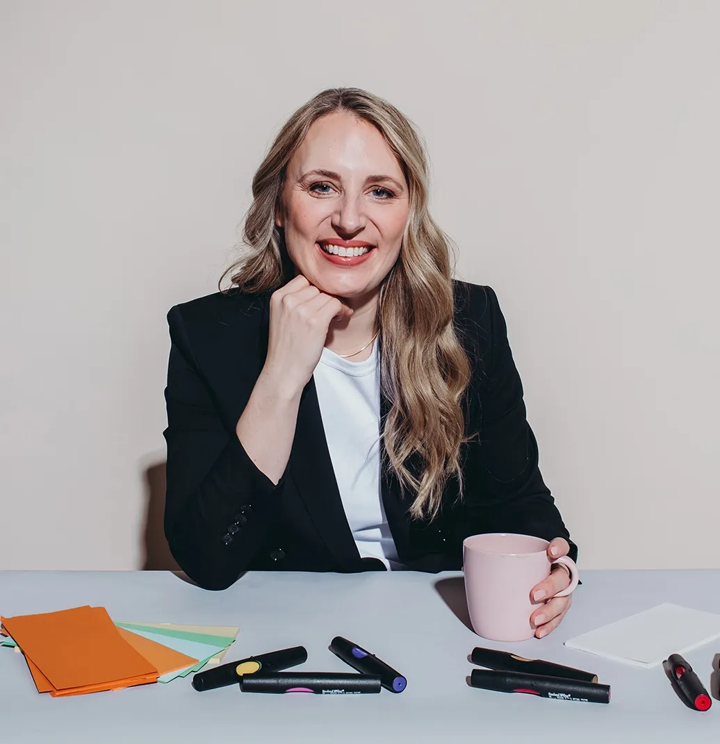 Melanie Bosse, lächelnd in dunklem Blazer an einem Tisch mit Coaching-Materialien und Kaffeetasse