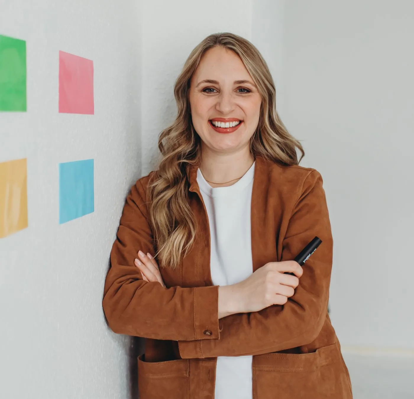 Melanie Bosse mit verschränkten Armen, lächelnd vor einer Wand mit bunten Klebezetteln