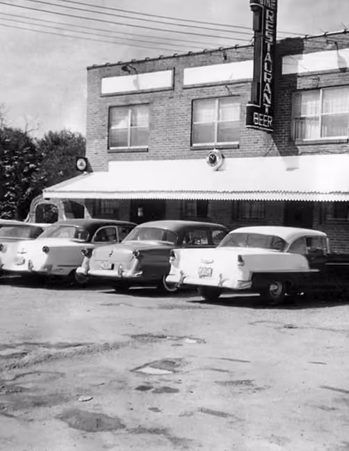 Four vintage cars parked outside a brick building with a sign reading 'Restaurant Beer'.