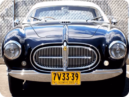 Front view of a shiny black vintage car with round headlights and a yellow New York license plate.