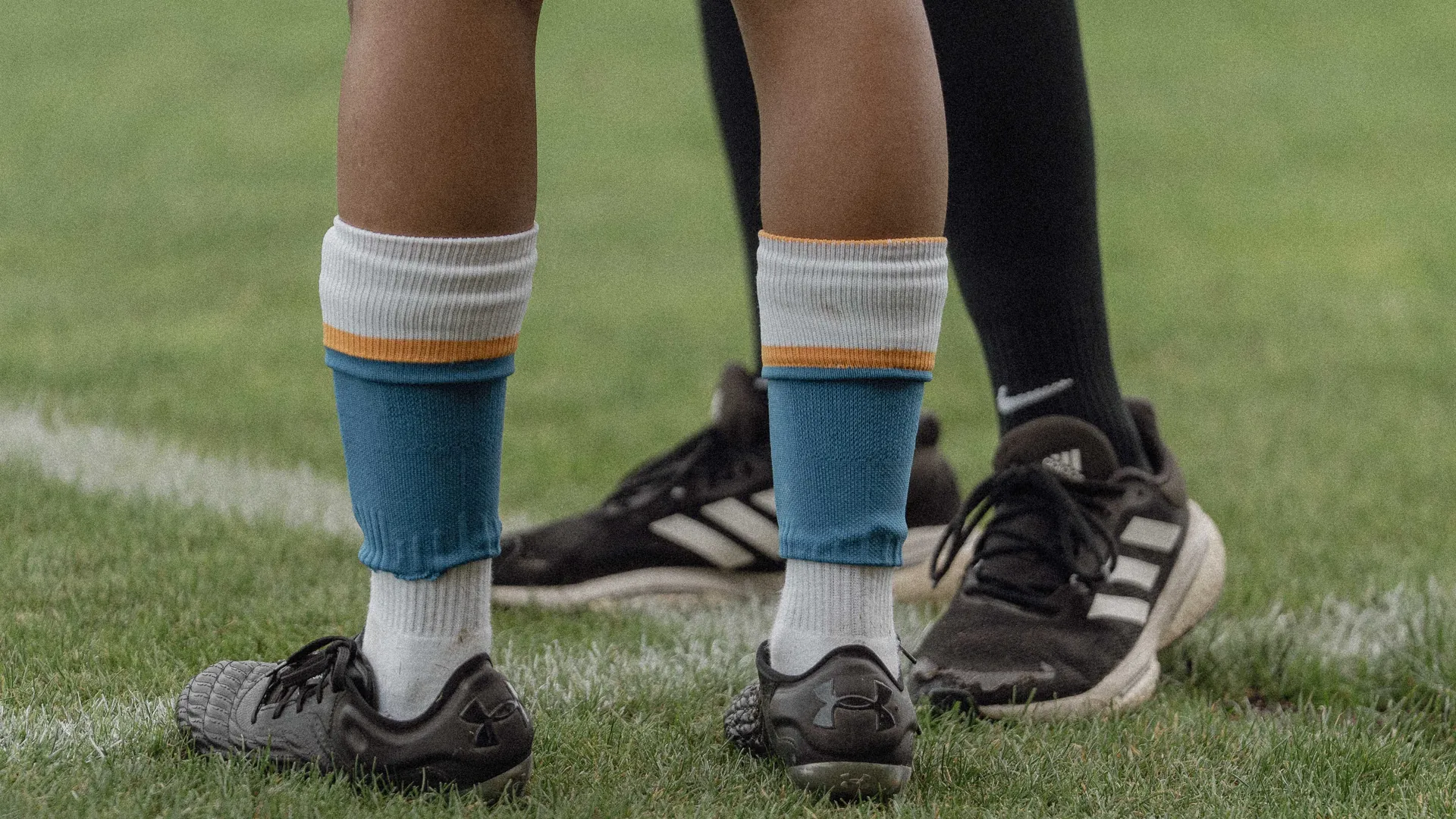 Jambes d'un athlète au bord du terrain, chaussettes et crampons sur la pelouse