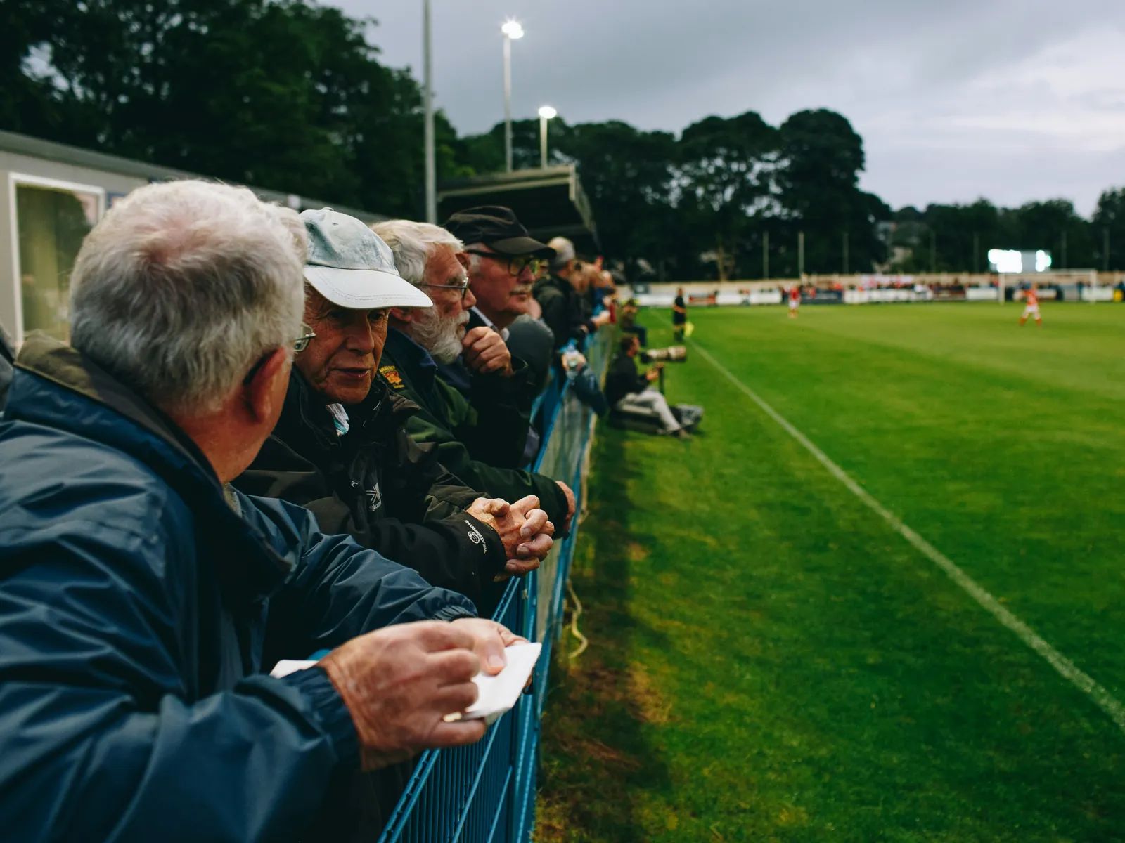 Bénévoles et supporters accoudés à la main courante d'un terrain amateur